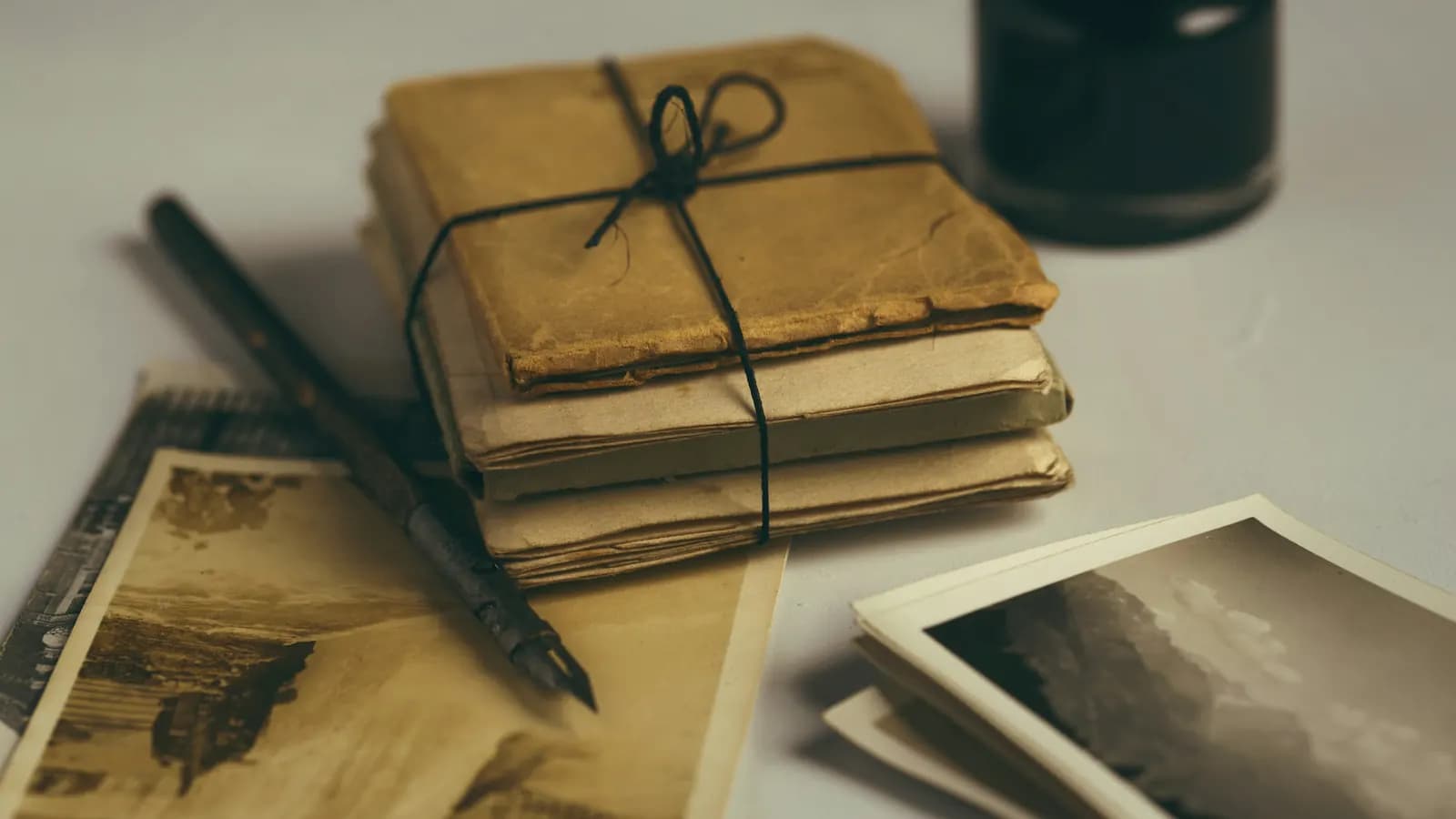 A bundle of old letters tied with string beside a dip pen, an ink bottle and old photographs