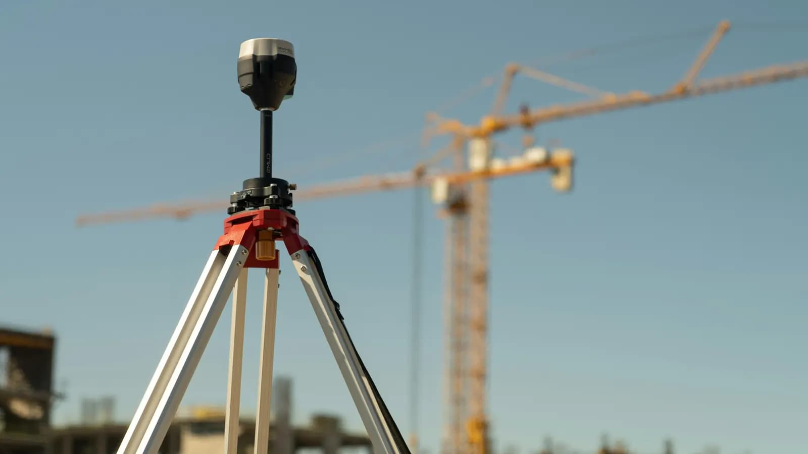 A surveyor's GPS receiver on a tripod in front of tower cranes on a building site