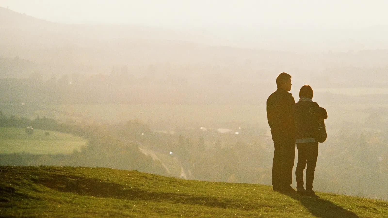 A couple, seen from behind, on a hillside looking out over a misty valley