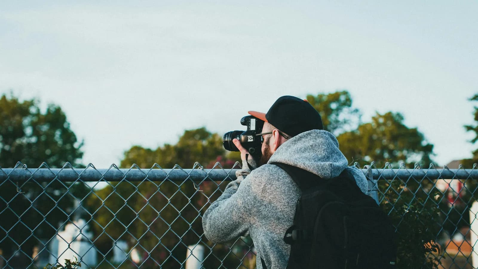A photographer, seen from behind, taking pictures over a chain-link fence