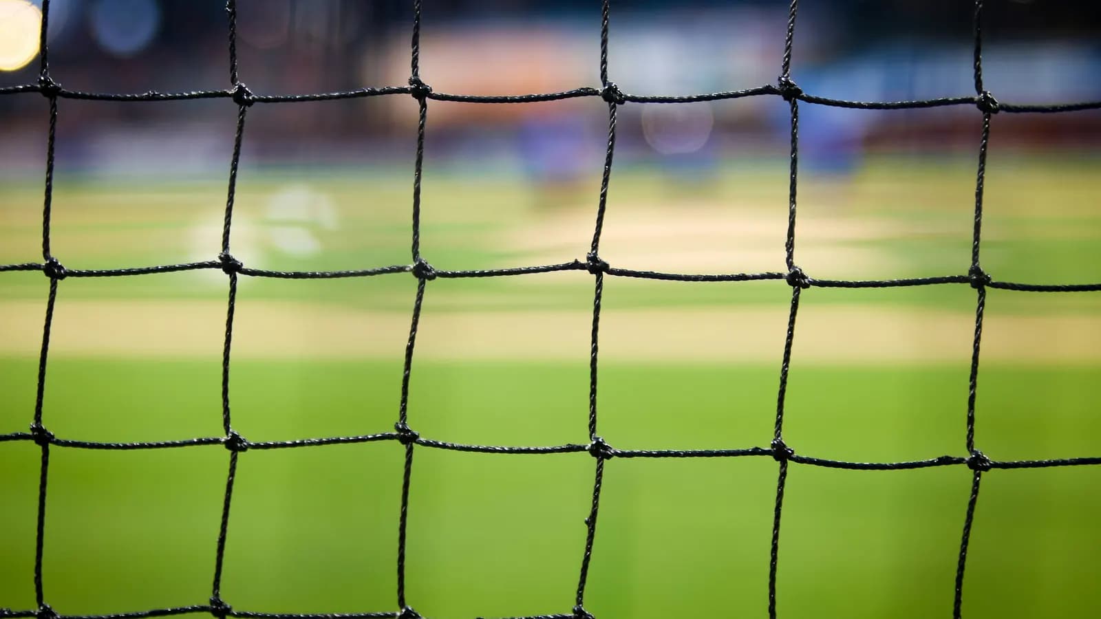 A close-up of a football goal net with a blurred green pitch behind it