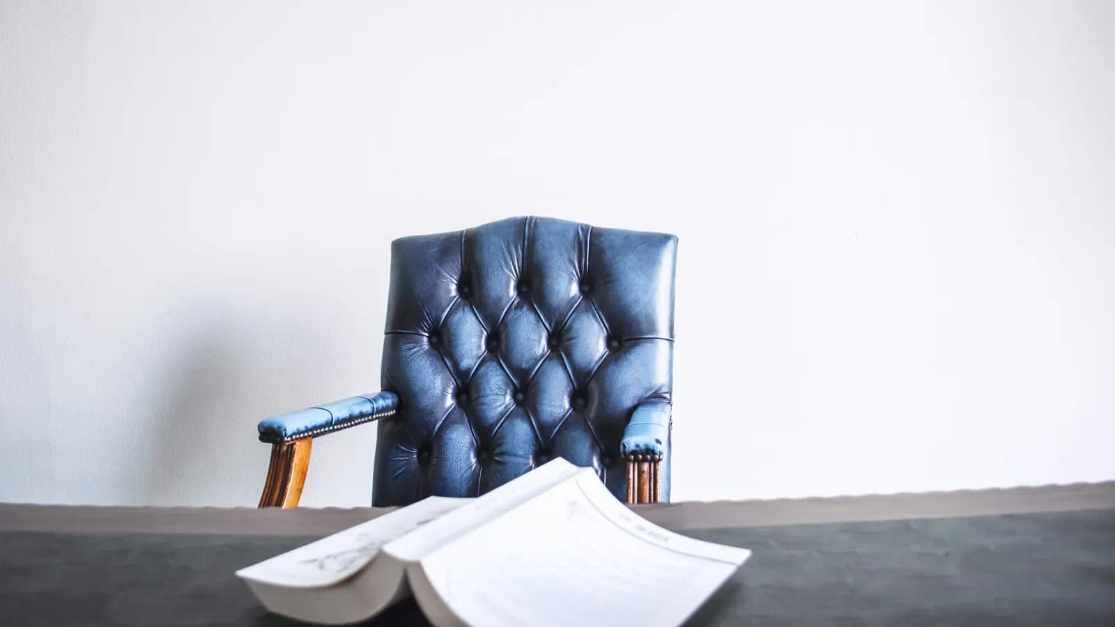 An empty buttoned leather chair behind a desk with an open document on it