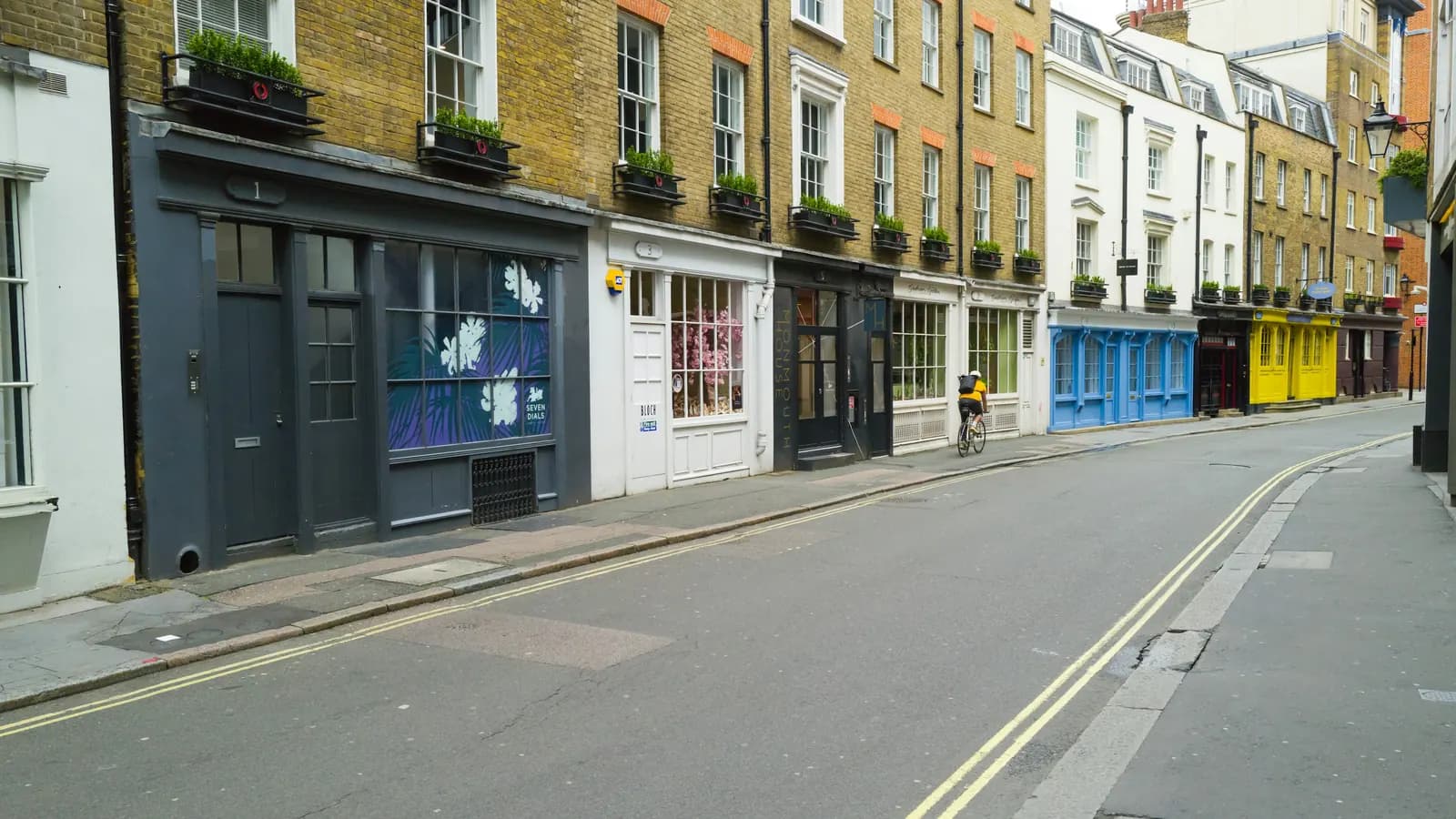A row of shopfronts beneath Georgian terraces on a quiet London street