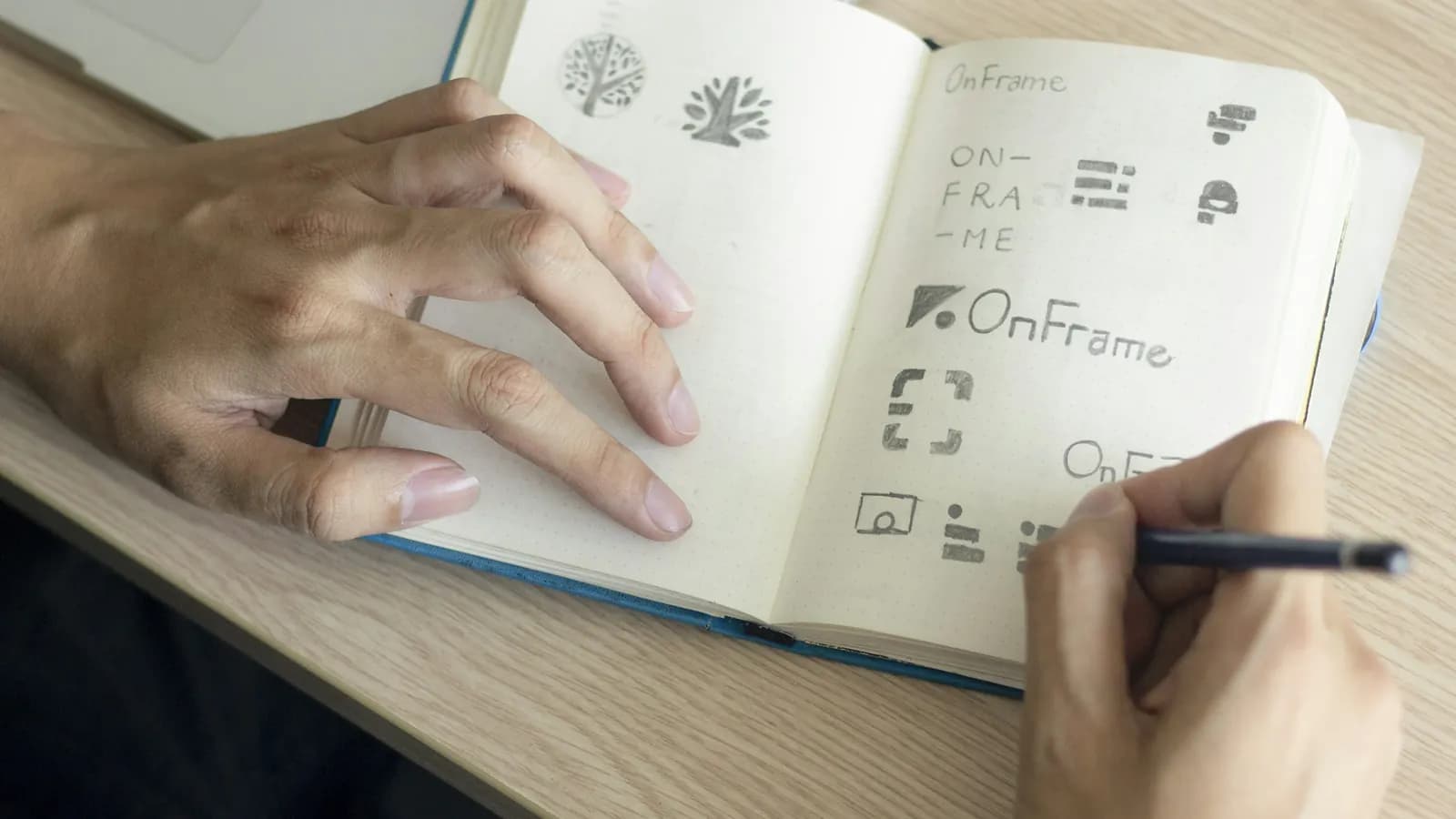 A hand sketching logo ideas for a new brand name in a notebook