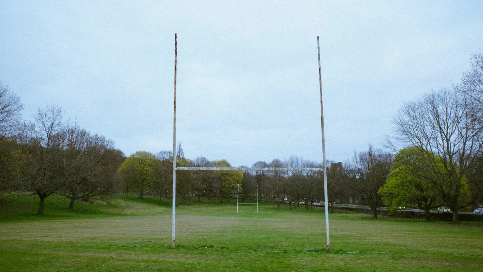 Rugby goalposts on an empty grass pitch lined with trees